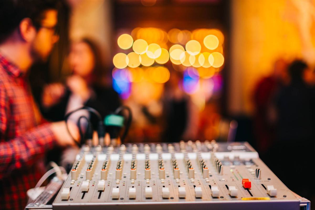 Nahaufnahme des Audio-Mischers mit unscharfem Hintergrund bei einer lebhaften Indoor-Veranstaltung.