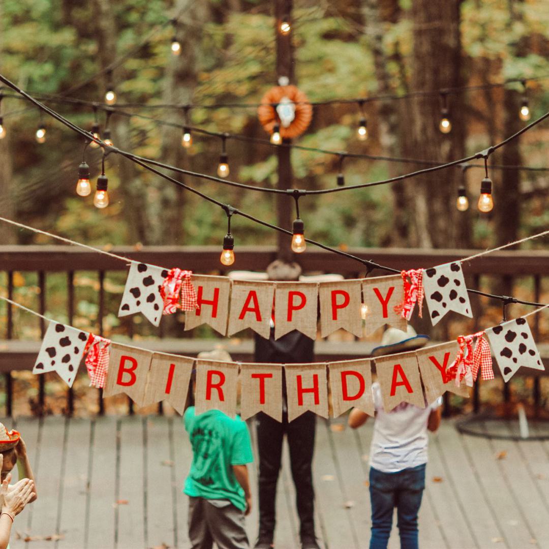 Menschen feiern einen Geburtstag und unterhalten sich - davor ein Schild mit dem Schriftzug "Happy Birthday" (in deutsch: Herzlichen Glückwunsch)