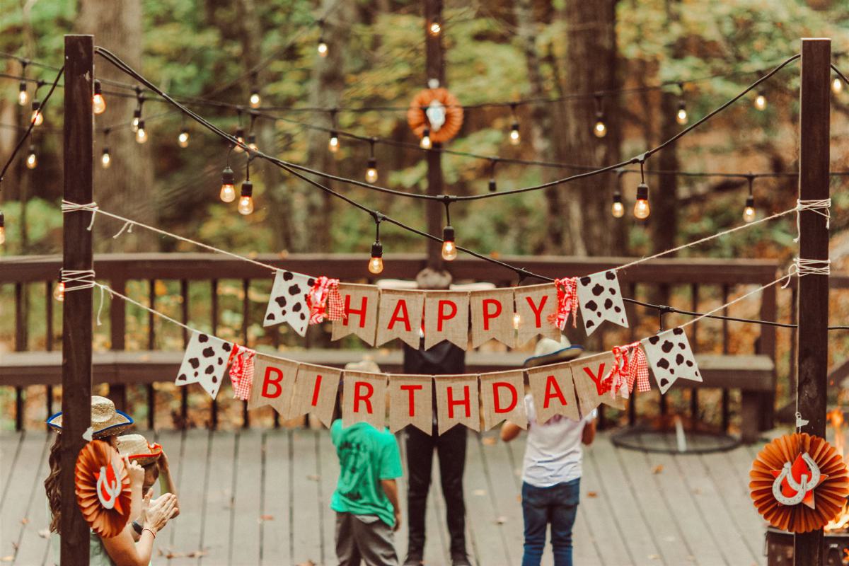 Menschen feiern einen Geburtstag und unterhalten sich - davor ein Schild mit dem Schriftzug "Happy Birthday" (in deutsch: Herzlichen Glückwunsch)