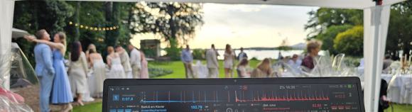 Blick vom DJ-Pult auf eine Sommerhochzeit im Schloss Golm bei Potsdam: Gäste feiern am Zernsee, dezente Musik und warme Abendstimmung.