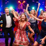 Gäste tanzen bei einer Familienfeier im Landkreis Dahme-Spreewald ausgelassen, DJ-Pult hinter den Tänzer mit Partybeleuchtung.
