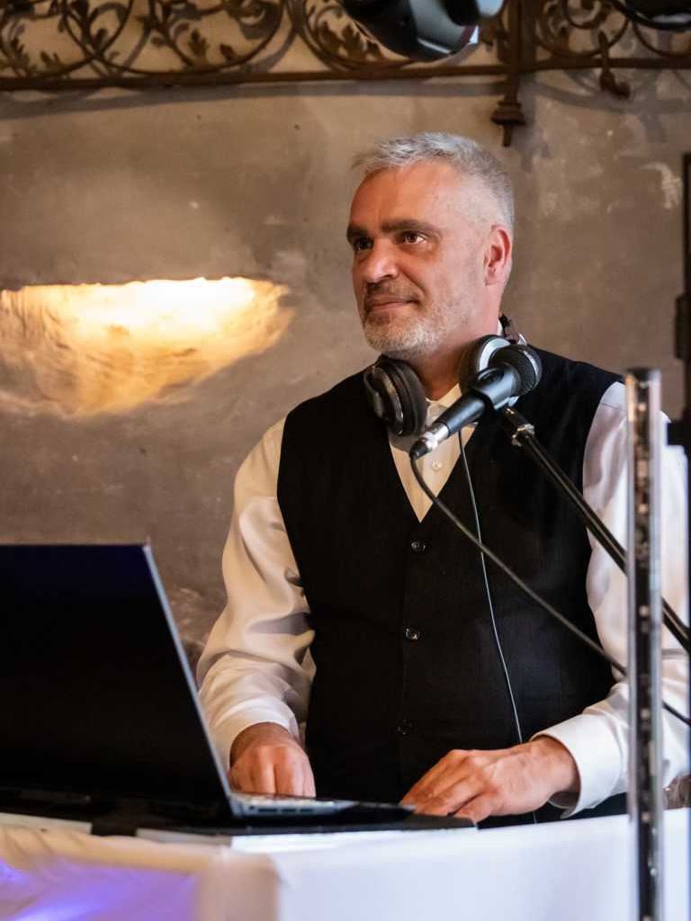 DJ Tom Joe steht bei einer Hochzeit auf Schloss Diedersdorf hinter sein DJ Pult und begleitet ein Hochzeitspiel.